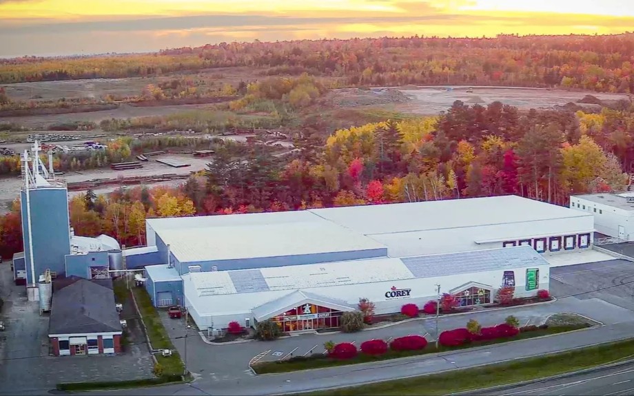 Aerial view of the Corey plant at sunset: white warehouse roofs, silo tower, retail storefront and autumn treeline