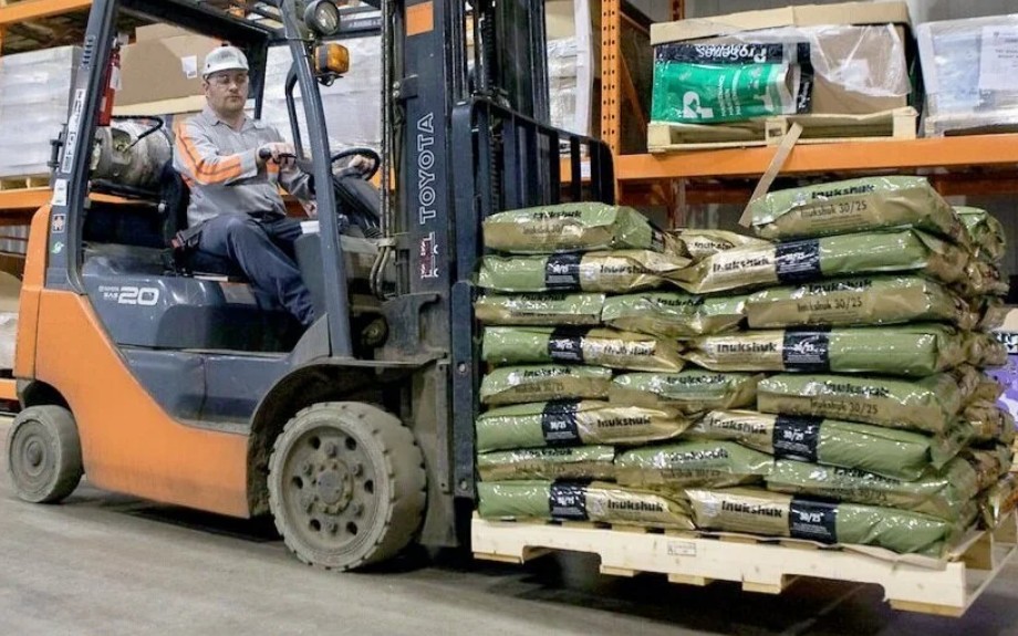Forklift operator moving a stacked pallet of Inukshuk 30/25 bags through warehouse racking