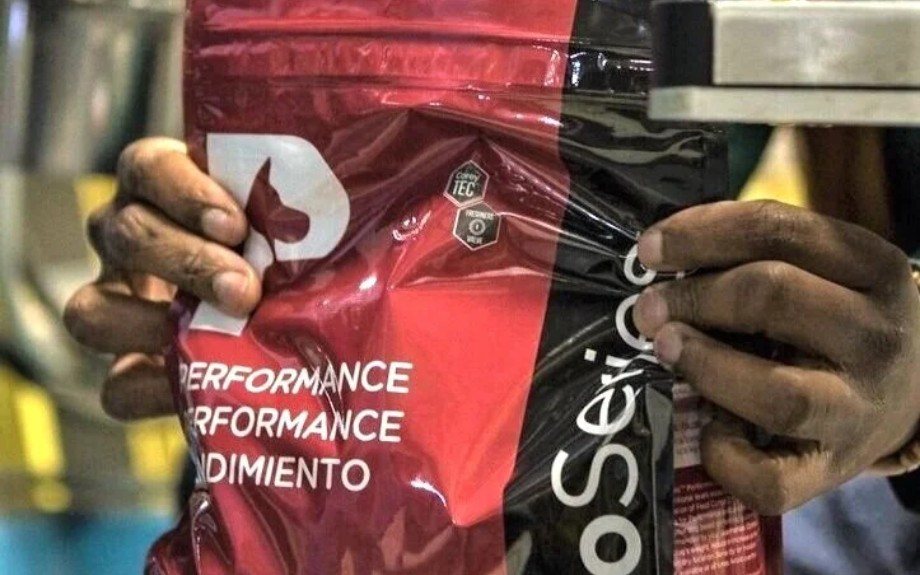 Hands holding a red Performance pouch with English and Spanish label copy at the packaging line